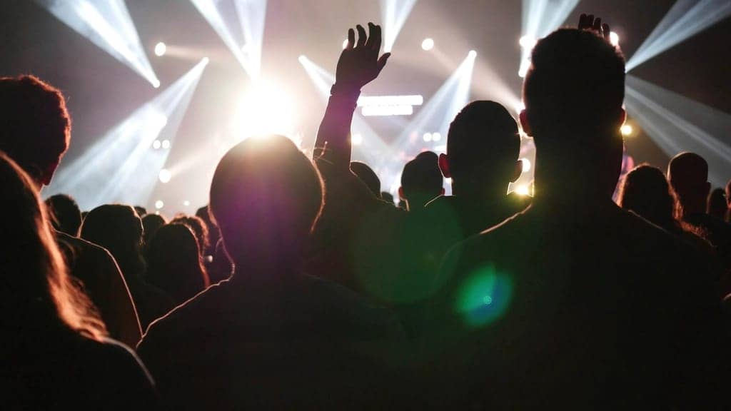 Silhouettes cheering with hands up in front of warm golden stage lights