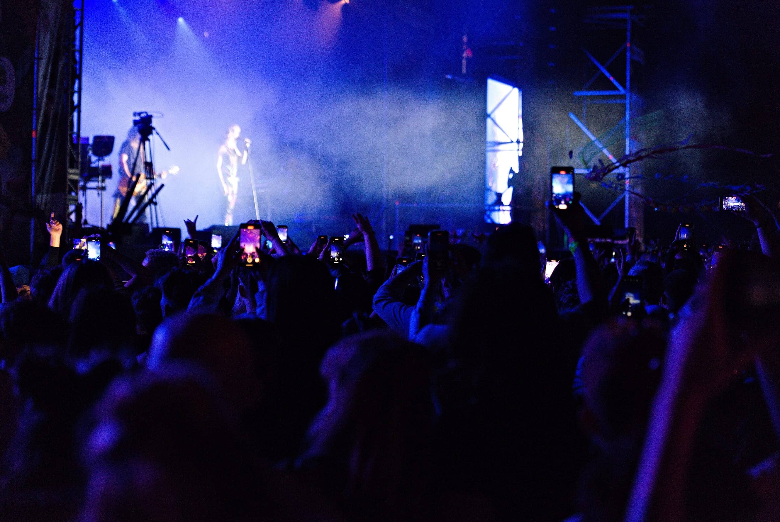 Silhouetted crowd with raised hands under violet and blue stage lights