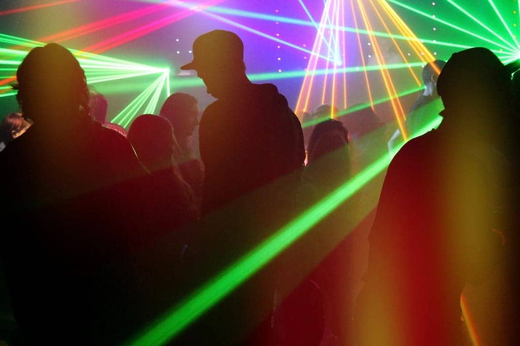 Partygoers in silhouette under green and pink laser beams